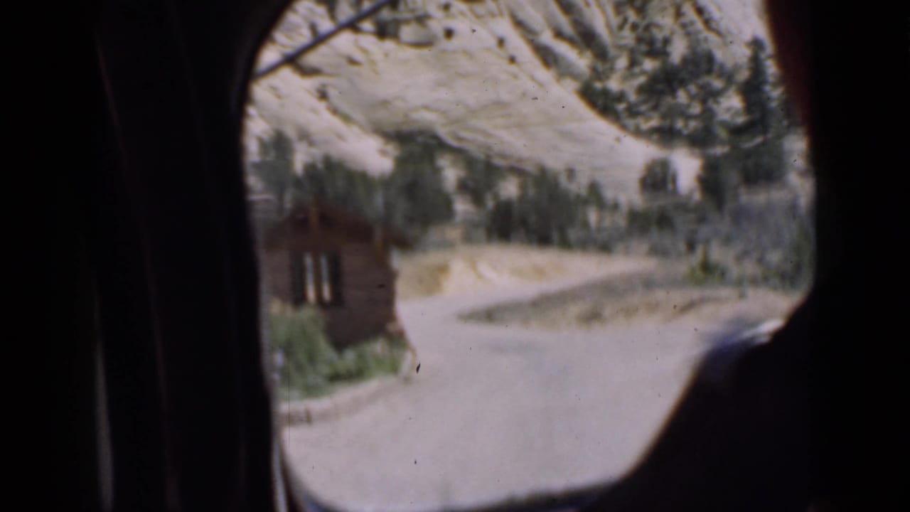 View through a car window toward a cabin and curving mountain road.