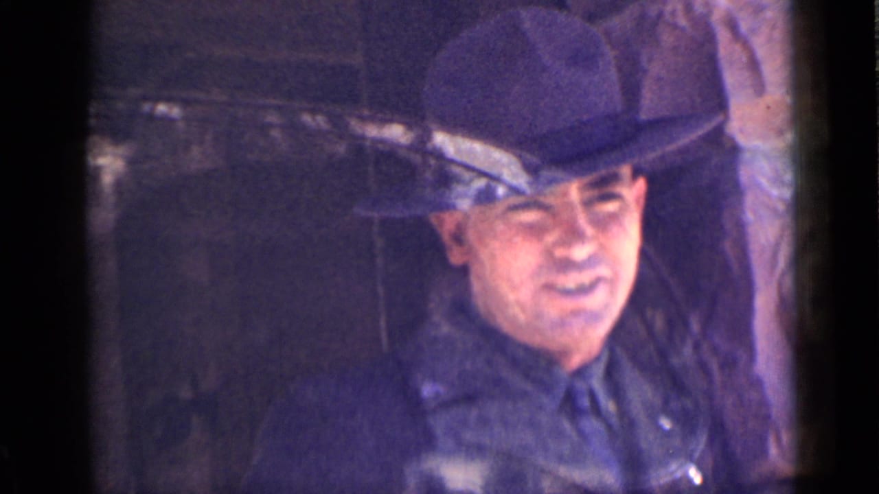 Uniformed man in a broad-brimmed hat seen through a dark window frame.