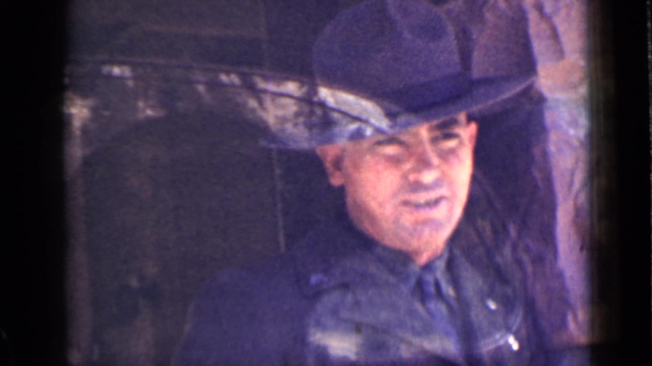 The likely ranger remains framed by the tower window, with his face visible under the brim of a wide hat in faded 8mm color.