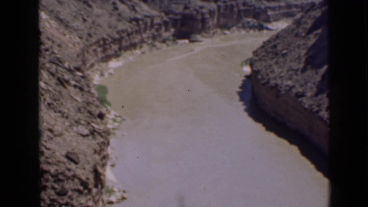Muddy river curves through a rocky canyon with steep dry banks.