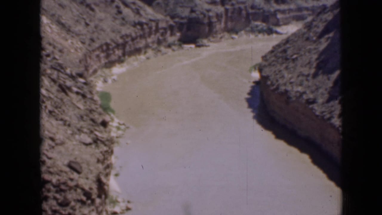 1939 Utah 8mm frame showing the broad muddy river channel below rough canyon walls and arid slopes.