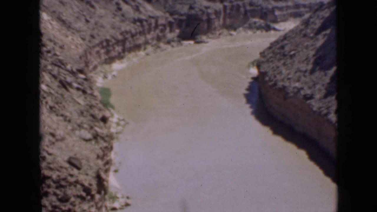1939 Utah 8mm frame of a winding muddy river between canyon walls, with shadow on one bank and sunlit rock on the other.