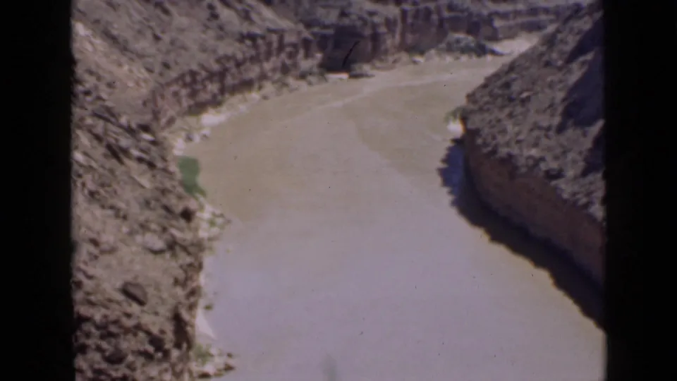 1939 Utah 8mm frame of a winding muddy river between canyon walls, with shadow on one bank and sunlit rock on the other.