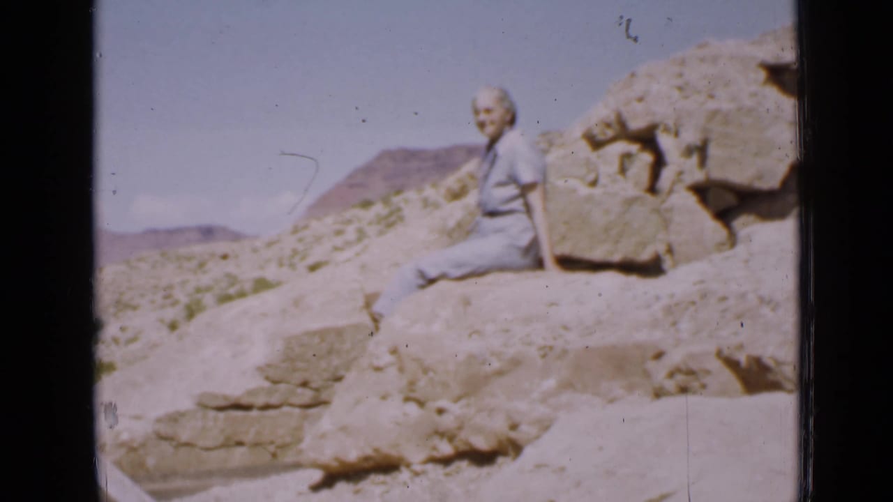Woman seated on rocks with a dry hillside and blue sky in the background.