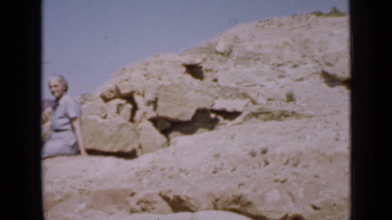 At the end of the 1939 Utah clip, the woman is partly framed at left beside pale rocks, scrubby ground, and an open blue sky.