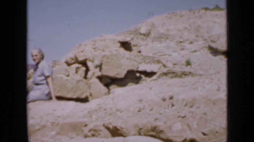 At the end of the 1939 Utah clip, the woman is partly framed at left beside pale rocks, scrubby ground, and an open blue sky.