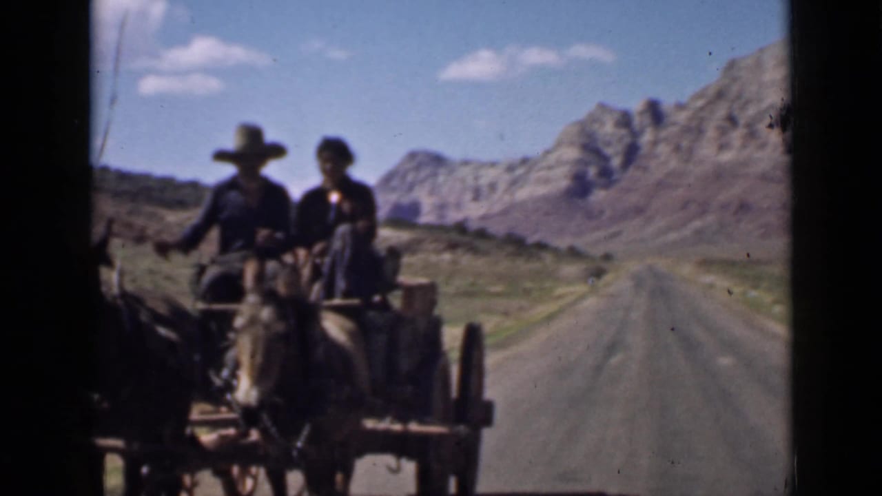 1939 Utah home-movie frame showing a horse-drawn wagon with two riders on an open road through mountainous desert terrain.
