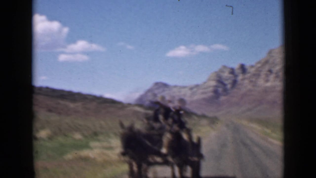 1939 Utah home-movie frame of a horse-drawn wagon traveling away on a road through open desert and mountain scenery.
