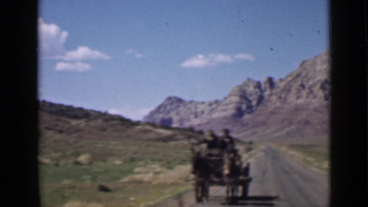 1939 Utah home-movie frame showing a distant horse-drawn wagon on a desert road with rugged mountains beyond.