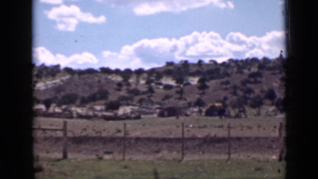 Wire fence in the foreground with shrub-covered hills and clouds beyond.