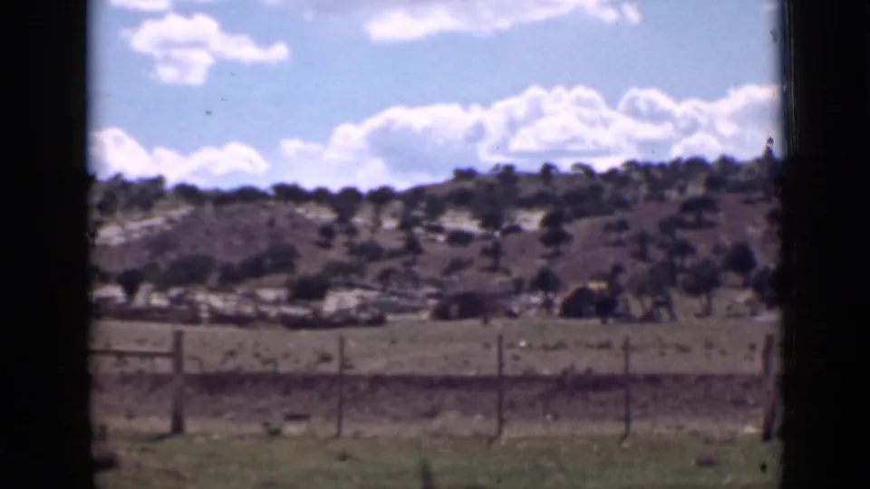 1939 Utah landscape view with a foreground fence, open pasture, scattered trees, low hills, and a bright blue sky.