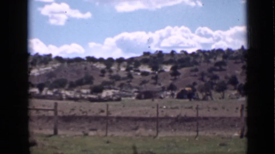 Final 1939 Utah home-movie frame of a wire fence, open ground, shrub-covered slope, and bright clouds within dark film borders.