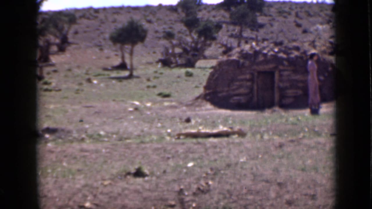 Rustic low structure in open arid terrain with a person standing nearby.