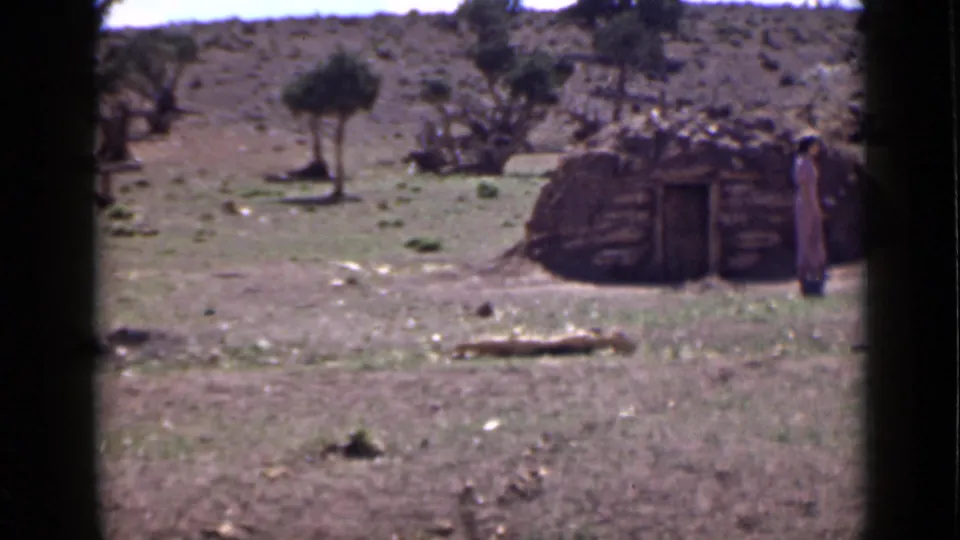 1939 Utah home-movie frame showing a small rustic structure, rocky ground, sparse trees, and a standing figure in an arid setting.