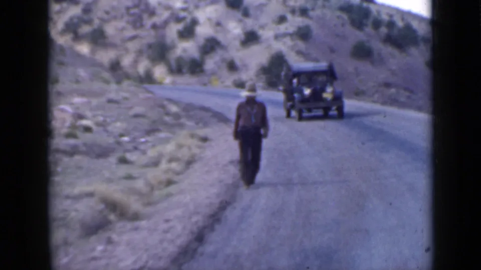 1939 Utah home-movie view of a man walking down a rural mountain road with an older dark car visible beyond him.