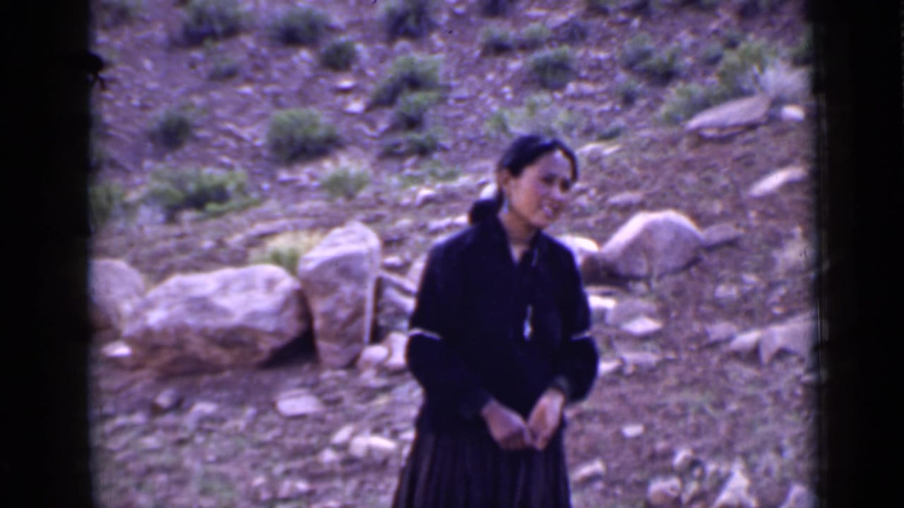 Young woman in dark dress looks slightly off-camera on a rocky Utah hillside, with boulders and brush behind her.