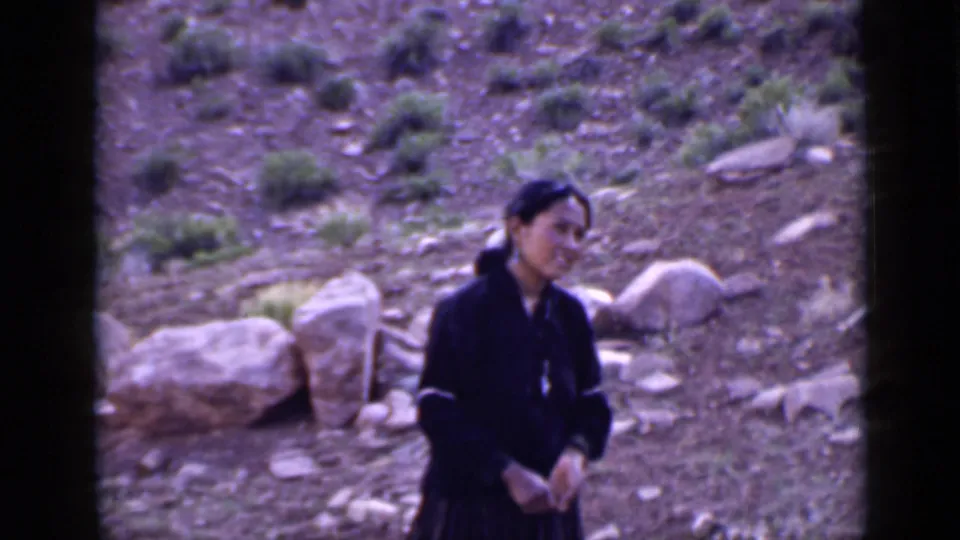 Young woman in a dark long dress stands near large rocks on a dry Utah hillside in 1939 8mm footage.