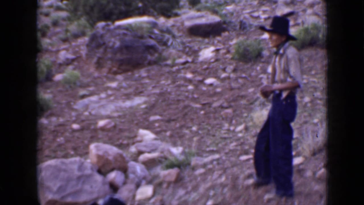 Man in a cowboy hat standing on a rocky hillside.