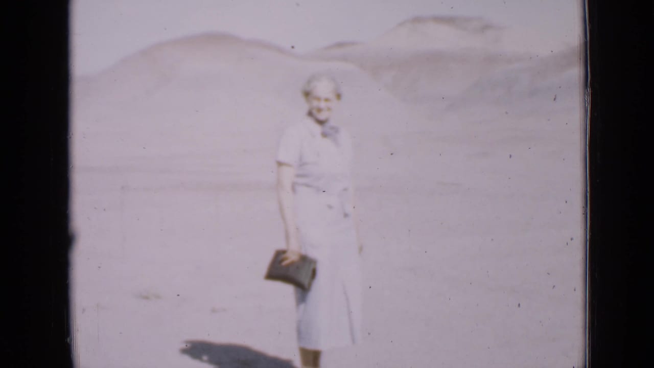 In 1939 Utah home-movie footage, an older woman in a blue dress stands in bright desert light with hills behind her.