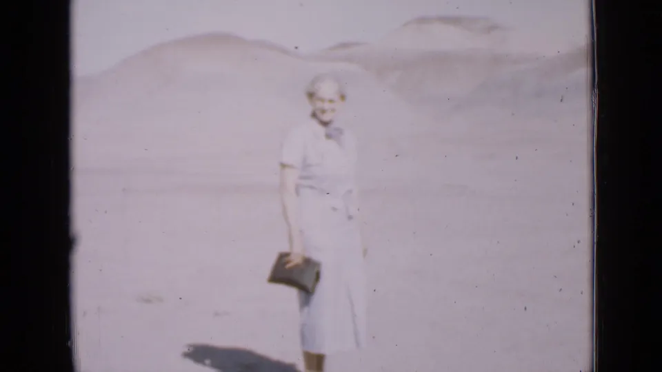 In 1939 Utah home-movie footage, an older woman in a blue dress stands in bright desert light with hills behind her.