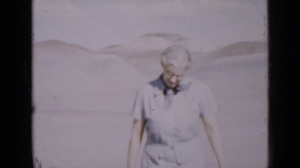 Older woman in light clothing walks through a Utah desert dune landscape in 1939 home-movie footage.