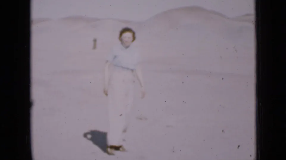 A woman in light blouse and trousers walks across a pale Utah desert dune area in 1939 8mm footage.
