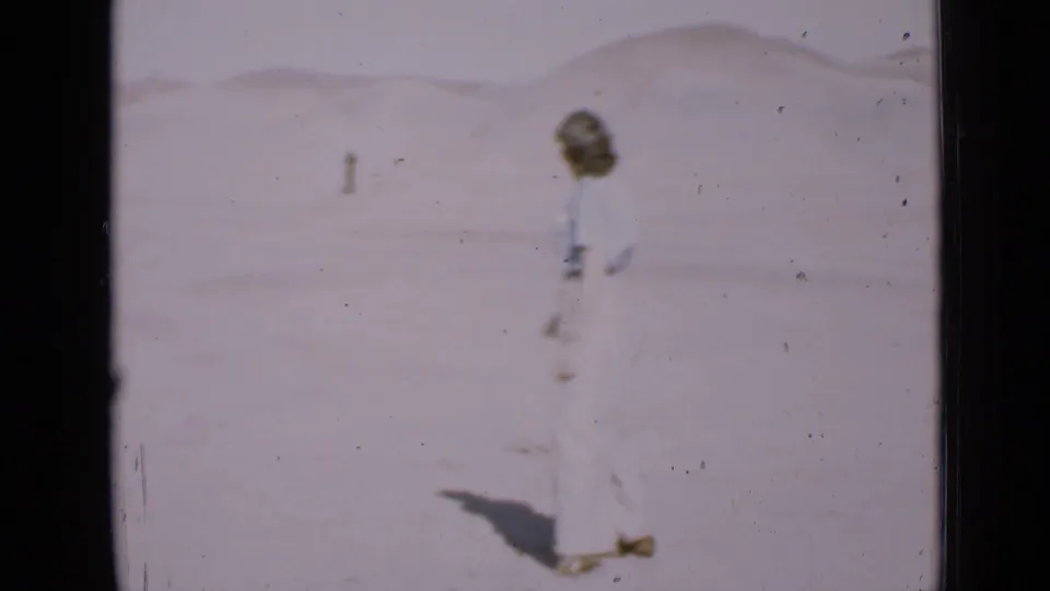 Woman seen in profile on bright desert sand in Utah, with a low dune line in the distance.
