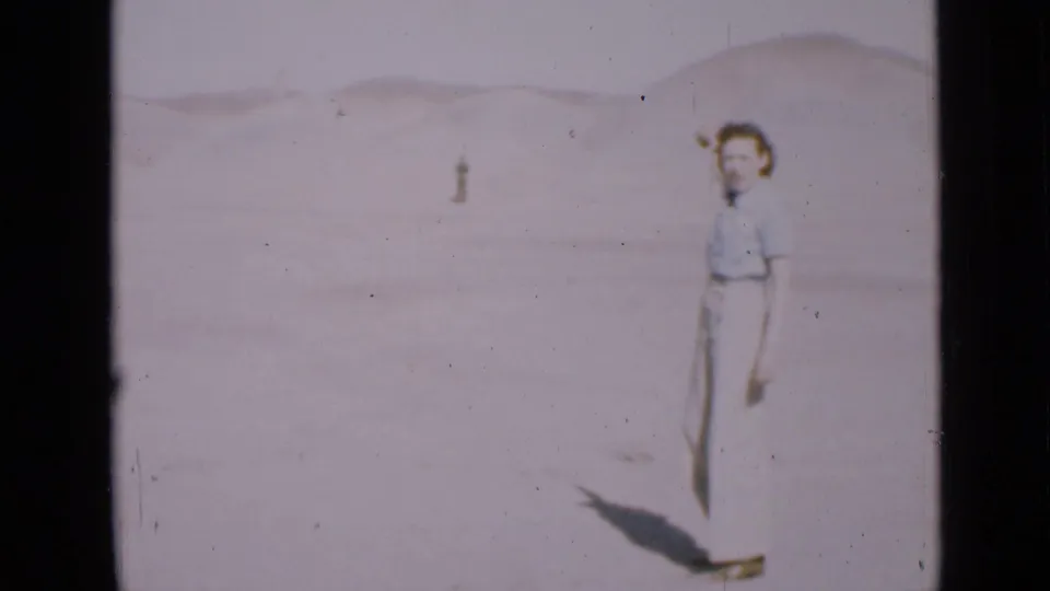 In 1939 Utah home-movie footage, a woman stands in a bright desert landscape while a distant person appears on the sand behind her.