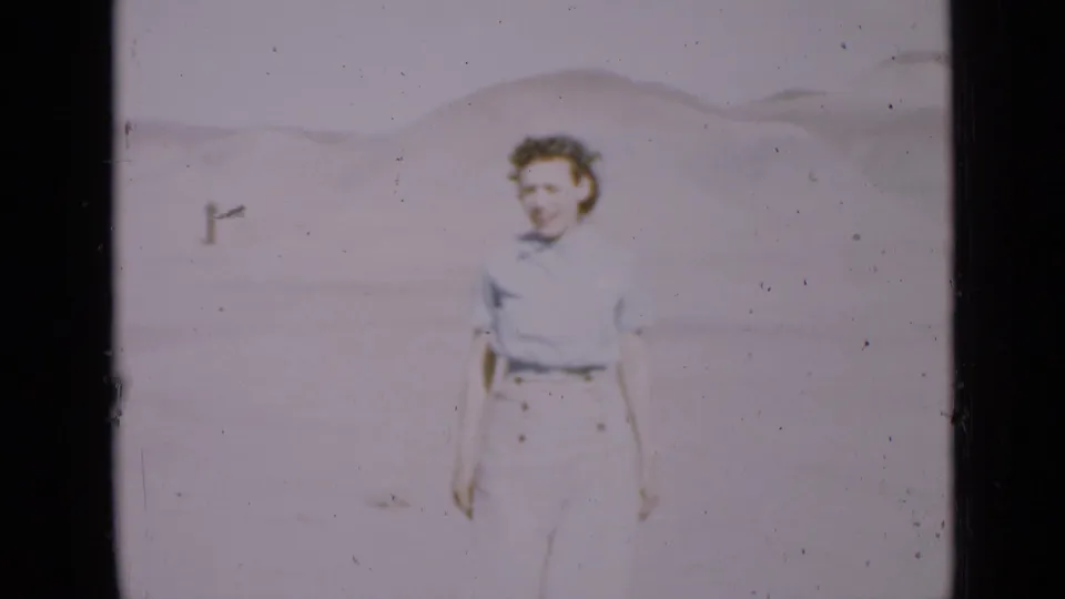 Young woman walks toward the camera across an open Utah desert, with pale dunes and hills behind her.