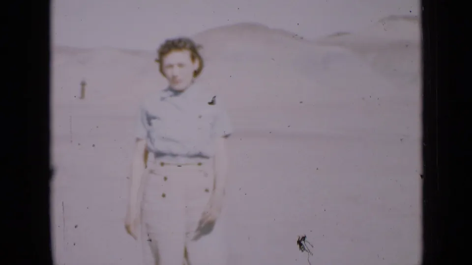 Closer 8mm frame of a young woman in a light blouse and high-waisted trousers against Utah desert dunes.