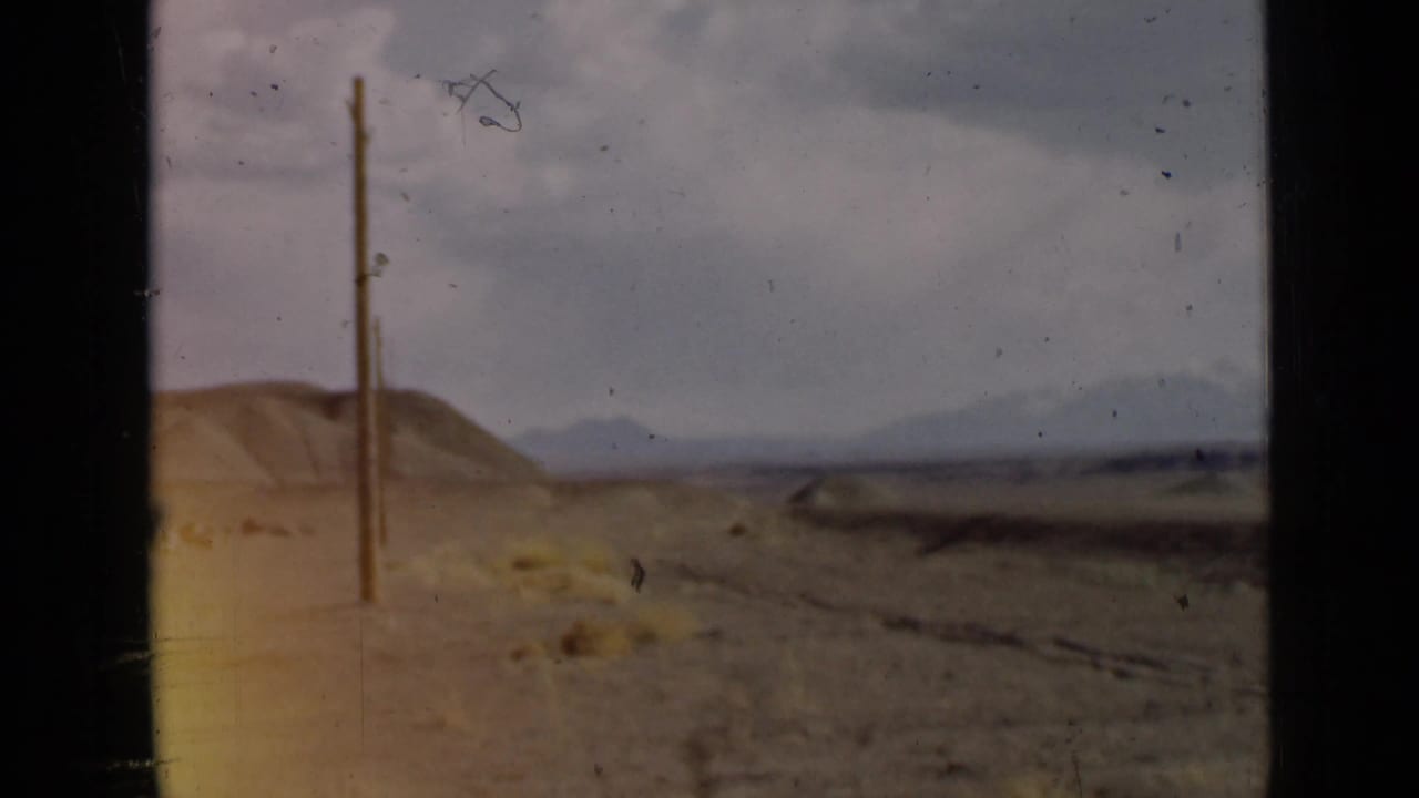 1939 Utah 8mm frame showing a muted desert plain, low hills, distant mountains, pale cloudy sky, and a vertical utility pole near the left edge.