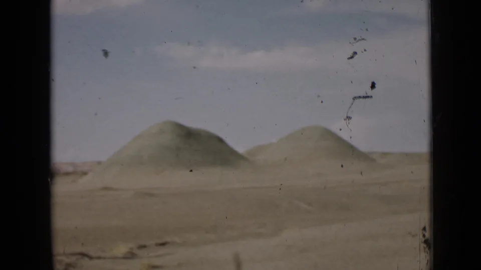 1939 Utah 8mm frame showing rounded desert hills across flat arid terrain, with muted color, pale sky, scratches, and dark frame edge.