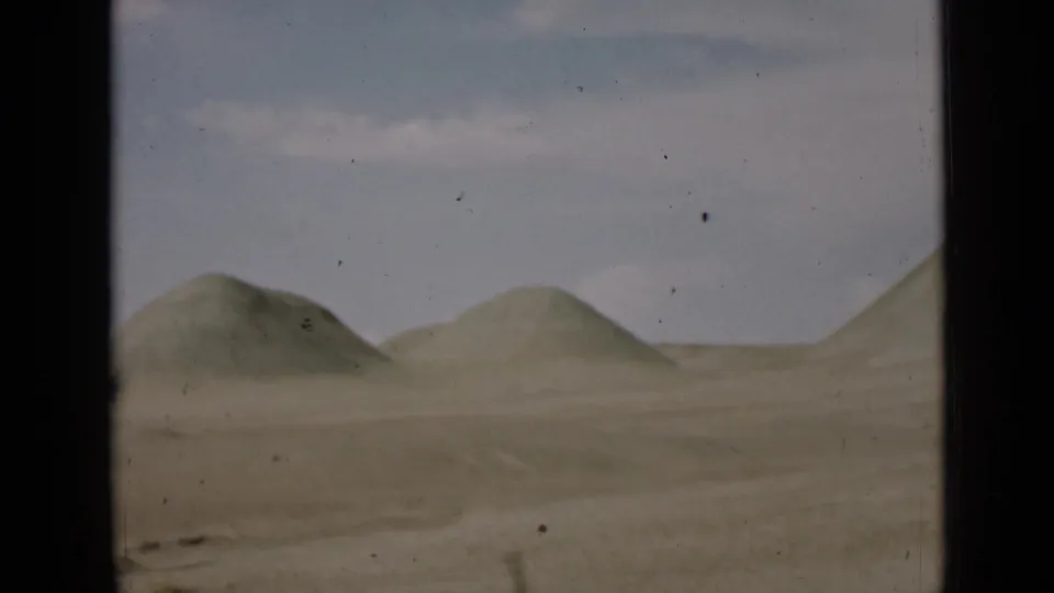 1939 Utah home-movie frame showing low desert sand hills and a flat foreground beneath a pale sky, bordered by dark 8mm film edges.