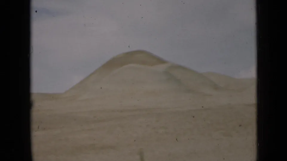 1939 Utah 8mm frame showing a larger sand hill and lower ridges beyond a flat desert foreground, with muted color and visible film wear.