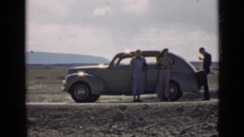 Travelers stand around a 1930s-style car in Utah, filmed from a distance with soft color and visible 8mm grain.