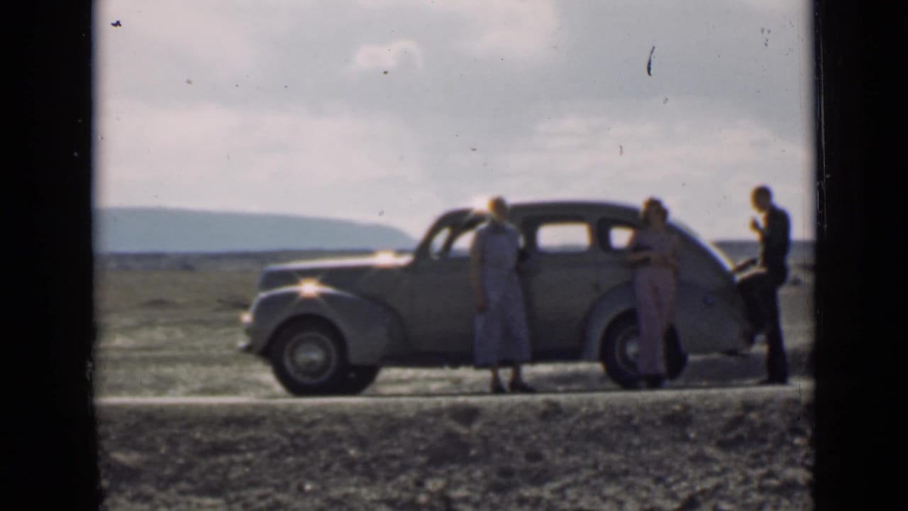 Three adults remain beside a rounded vintage sedan on a Utah roadside, with an open horizon and low hills in the background.