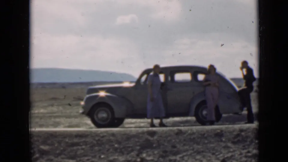 A woman stands near the sedan door while another adult and a man are positioned by the rear on a rural Utah road.