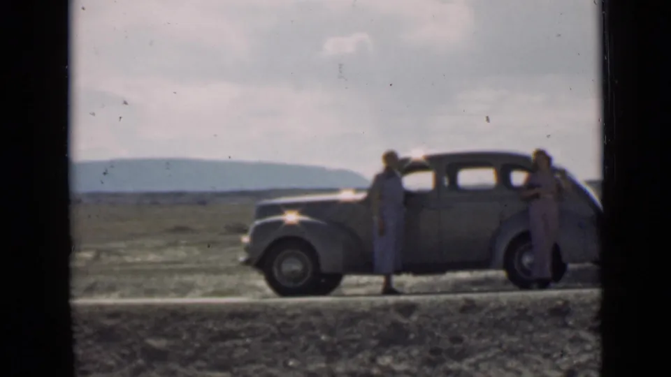 By the end of the 1939 Utah clip, two adults are clearly visible near the parked sedan against a broad roadside landscape.