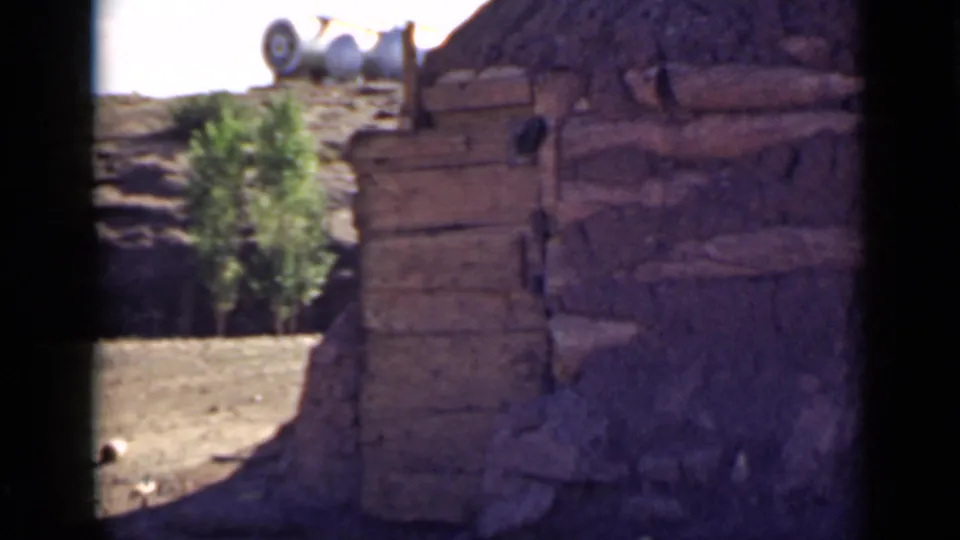 The camera shows a weathered mud-walled structure in Utah, with exposed wooden beams, a small tree, and bright desert light.