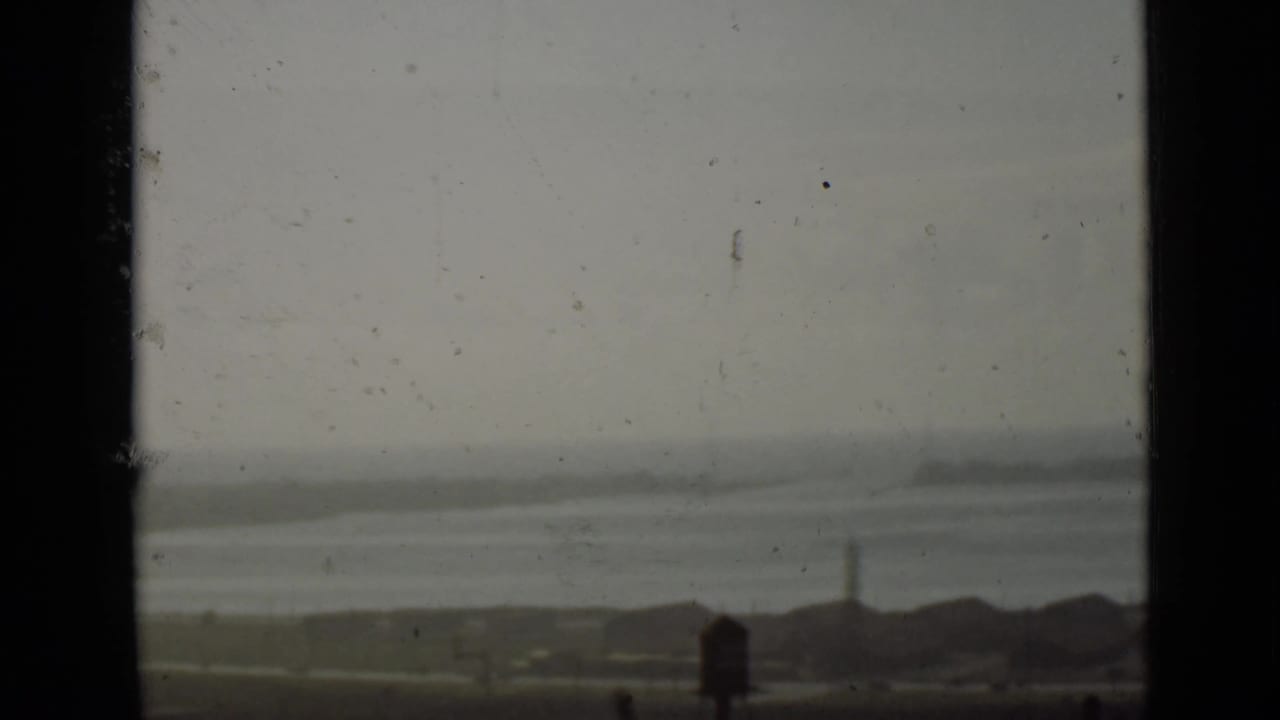 Distant hazy water and shoreline seen through dark vertical frame edges.