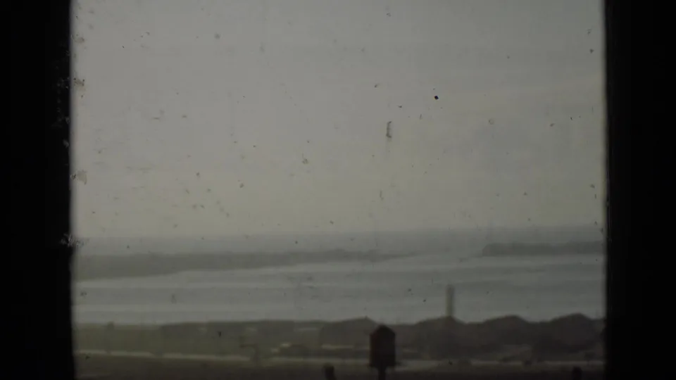 1940 Ontario 8mm view of hazy water, a low shoreline, and distant structures framed by dark window or film edges.