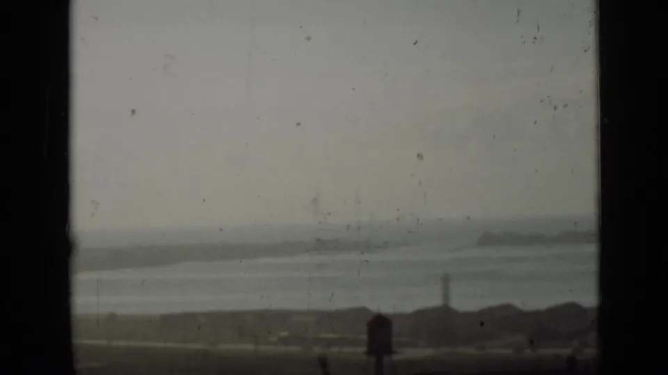 Distant Ontario waterfront view with water, low structures, and a tower visible through a dark-framed opening.