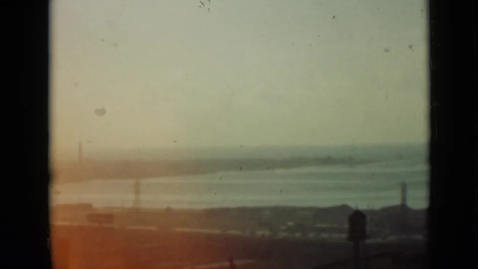 1940 Ontario 8mm frame showing a washed, hazy view over calm water and distant shoreline, with a dark foreground and orange film flare below.