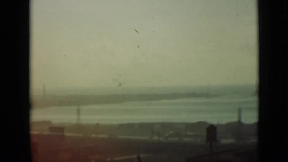 1940 Ontario 8mm frame with a soft elevated view across calm water, distant pylons and buildings, and a dark foreground edge.