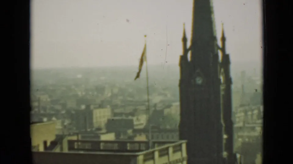 1940 Ontario home-movie frame showing a dark Gothic-style clock tower beside a flagpole over a hazy city view.