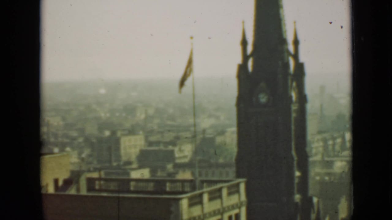 Clock tower at right, flagpole near center, foreground building roof, and distant city haze.