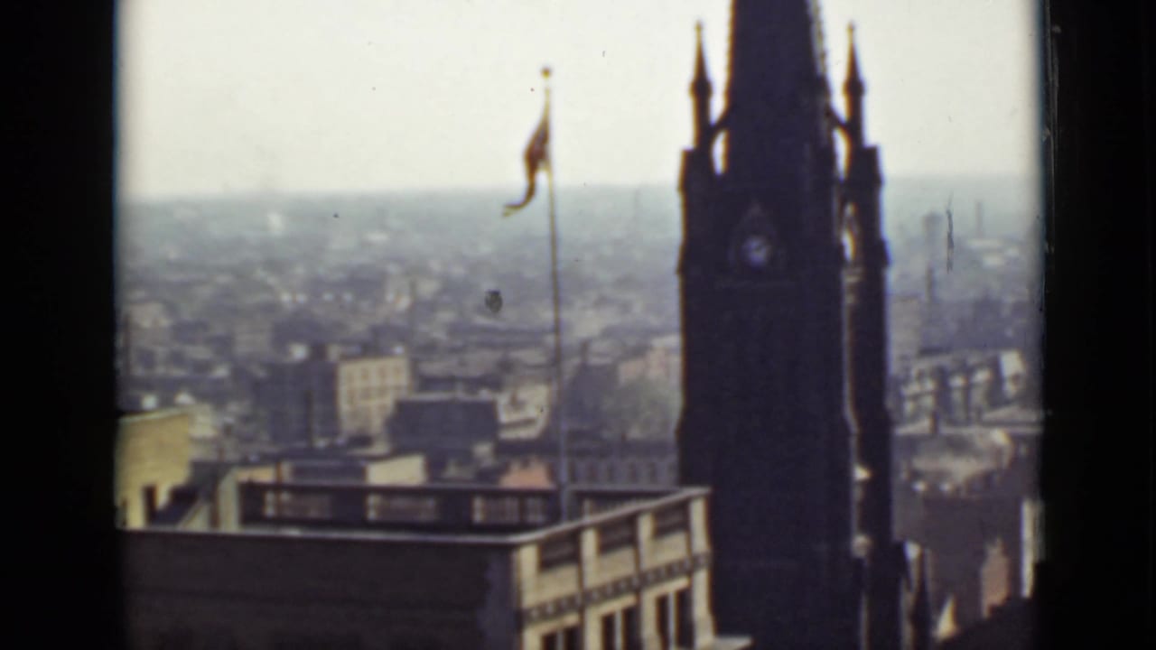 High view of a tower, flagpole, rooftops, and distant city skyline.