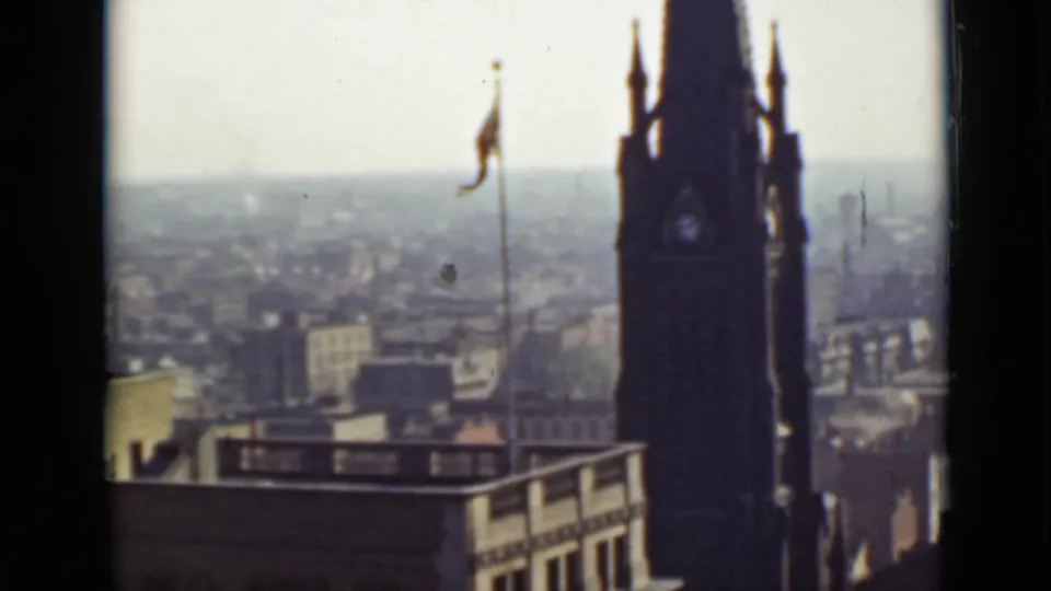 High-angle 1940s Ontario home-movie view of a tower silhouette, flagpole, rooftops, and hazy urban skyline.