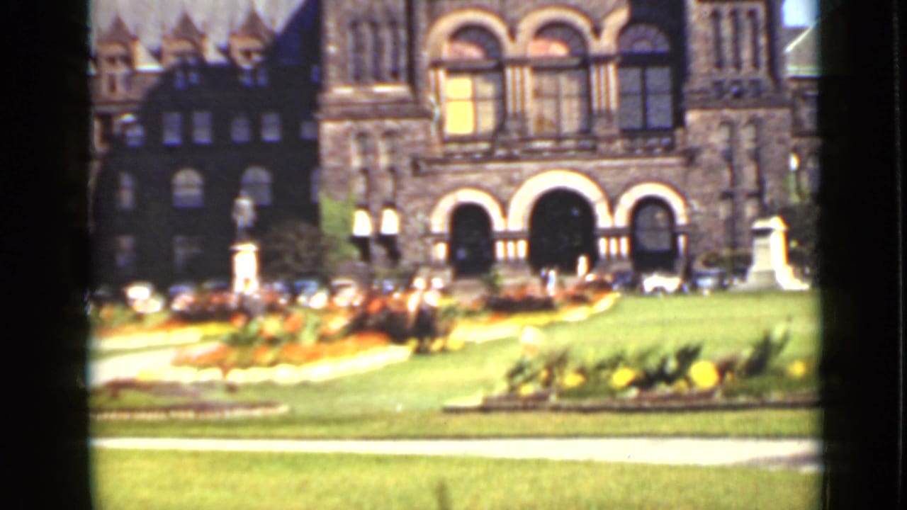 Stone building with arched entrances behind flowerbeds and lawn.