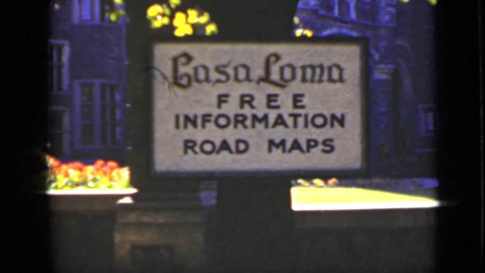 1940 Ontario 8mm frame showing a Casa Loma sign with free information and road maps text near flowers and dark building details.